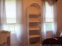 Full view of the white wicker shelf in front of windows with curtains.