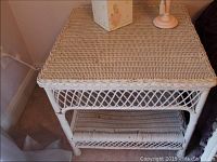 White wicker end table showing woven top and bottom shelf with crisscross apron design.