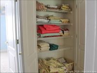 Closet shelving showing folded linens including towels, pillow cases, tablecloths, and blankets in various colors and designs.