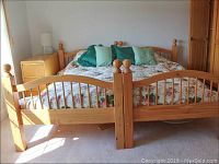 Photo of two solid wood twin beds combined to form a queen-sized bed with floral bedding and multiple pillows.