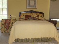 Front view of the queen bed made with linens and pillows, showing bedspread and draped side table.