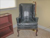 Front view of dark blue leather wing back chair showing shape, color and condition of upholstery and wooden legs.