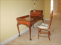 Angle view of wood desk with drawers and ladderback chair with floral cushion, showing the full desk and chair height and condition.