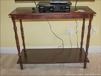 Front view of a wooden two tier table with dark finish, showing the top surface and lower shelf, with turned legs.