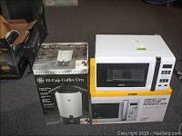 Photo of boxed Bella microwave oven stacked on GE 42-cup coffee urn boxed unit on carpet floor.