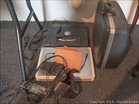 Photo of two Dell laptops stacked on floor with Kindle, two external hard drives, and Canon AE1 camera with lens cap and strap.