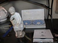 Lladro girl figurine next to Wedgwood state seal plates in box and Hutschenreuther Bermuda plate booklet