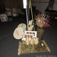 Wide shot of all items arranged on a floor including hat boxes, floral vase, silk door mat, frames, lampshades, and wall decorations