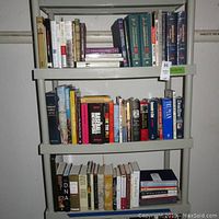 Bookshelf with three shelves filled with mostly hardcover books, bottom shelf not included.