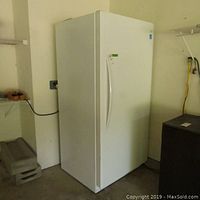 Front view of white upright freezer with handle, showing minor dents and scratches on the side panel.
