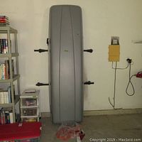 Grey Volvo cargo box vertically mounted on wall with attached black roof racks in garage, showing full length and width.