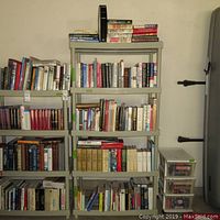 Five shelves filled with various books in different sizes and colors, items stacked upright and some horizontally on top of shelf.
