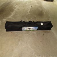 Closed black carrying case for Quik Shade Instant Canopy on concrete floor.