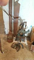Photo showing antique dual action pump, rusty lantern, large rusty hand saw and pitching horseshoes
