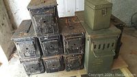 Stack of metal ammunition boxes showing multiple black and green boxes, several with rust and worn surfaces.