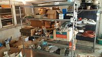 Garage shelf with mixed electrical and hardware items including boxes, bags, and coils of cords.