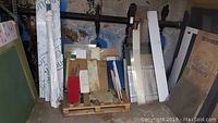 Wide view of multiple plexiglass sheets and other plastic sheets stacked vertically and horizontally on a pallet and leaning against walls.