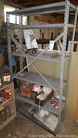 Full view of metal shelving unit holding various items including pumps and electronics in basement area.