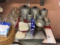 Overview of lot items on a red cloth including aluminum canisters, glass jars, Brita filters, trays, loaf pans, and other kitchen utensils.