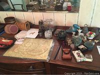 Wide view of tabletop showing lace doilies, coasters, fishbowl, playing cards, matchbooks, paper bookmarks, and various small figurines.