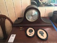 Front view of Sessions mantle clock with winding keys, alongside two small framed silhouette portraits in round frames against a wall.