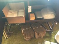 Overview showing a cardboard box with flattened boxes or inserts, plastic storage pouches, small yellow boxes, and two bundles of folded corrugated cardboard pieces under a wooden table.