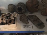 Overview of assorted primitive terracotta masks and stone tools on shelf