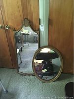 Photo showing both oval and rectangular mirrors together leaning against a wooden cabinet with the oval mirror in front.