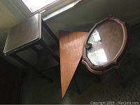 Three wooden end tables; one oval table with glass inset tray on top, triangle wooden table, and square wooden table with glass top and shelf underneath.