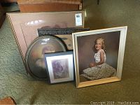 Five framed portrait artworks grouped on carpeted floor showing a variety of sizes and frame styles