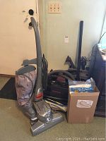 Kirby upright and Oreck canister vacuums standing on carpet with accessories piled behind