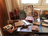Full view of the lot showing multiple vintage cigar boxes, boxed UpWords and Twixt board games, horse figurines, assorted buttons in a box, old photos, a green glass dish, and a brass or copper planisphere.