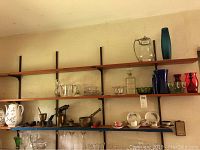 Shelf with brass items, ceramic pitchers, bone china tea cups and saucers, and glassware