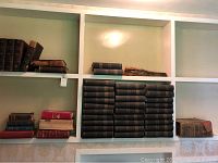 Wide view of shelves with multiple hardcover books arranged including large set of Encyclopedia Britannica volumes and other antique books.