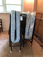 Two folded twin cots with mattresses on black metal frames and casters