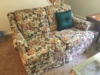 Front view of the loveseat showing floral upholstery and green accent pillow.