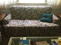 Full front view of three cushion floral sofa with window background and glass table in front.