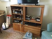 Full view of the oak media console showing glass doors, shelves, and open space for TV with various items inside and on top.