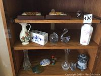 Photo showing wooden shelves with framed embroidery, ceramic vases, art glass paperweights, and small decorative figurines.