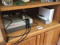 Nintendo Entertainment System (NES) and Nintendo Wii console placed on an entertainment center shelf.