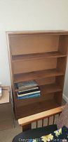 Front view of one wooden bookcase with four shelves and some books inside, showing overall structure and wood finish.