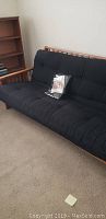 Wooden frame futon with black cushion mattress, showing tufted button design and slatted wooden sides and back