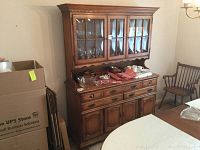 Front view of two-piece Pennsylvania House hutch showing glass doors with displayed glassware and lower storage with drawers and cabinet doors. Includes visible dining chairs and table nearby.