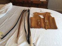Steer Brand tan leather vest with fringe and seven various women's belts on a white bedspread.