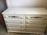 Front view of white painted Dixie Furniture Co. 8-drawer dresser showing floral design on top drawers and round knobs.