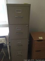 Full front view of the metal filing cabinet showing four drawers, metal handles, and label holders with lock on top drawer.