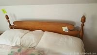 Front view of queen size wooden headboard attached to bed frame with white bed linens partially visible.