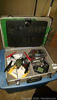Open silver carrying case with RC helicopter parts, remote controller, red and black propellers, manuals, and other small components inside.