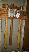 Three wooden baseball bats hanging on wall-mounted rack, view of entire bats and mounting hardware.
