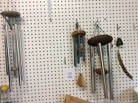 Four wind chimes hanging on pegboard, showing variety in size and style including metal tubes and natural branch design.